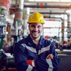 Smiling caucasian energy plant worker dressed in working clothes and with helmet on head standing with arms crossed.